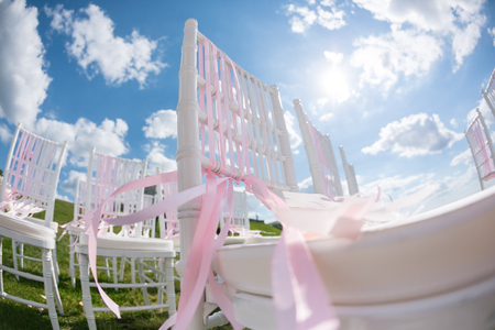 tapes fly in the wind. Romantic wedding ceremony. White wooden chairs with ribbon and flowers on a green lawn. Nice armchairs for guestsの写真素材