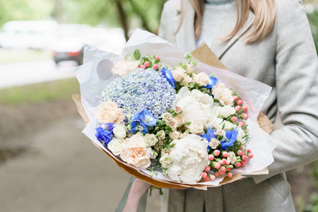 Young girl holding a beautiful spring bouquet. flower arrangement with hydrangea and peonies. Color light blue. The concept of a flower shop, a small family businessの写真素材