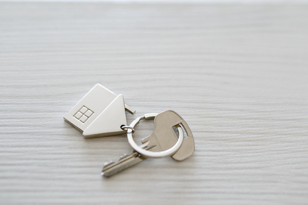 Mortgage concept. Key with house keychain on wooden table. Modern light lobby interior. Real estate, moving home or renting property.の写真素材