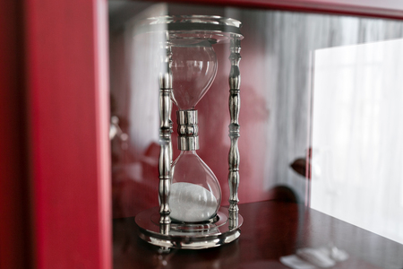 Close up of sand falling in sandglass or hourglass. Metal frame in the box behind the glassの写真素材
