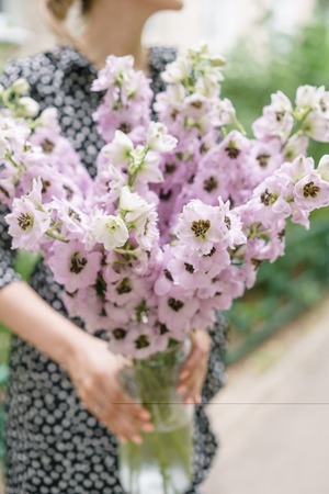 Young girl holding a flower bouquet with Delphiniums of lilac color in glass vase. Summer wallpaper. Selective focus. Flower shop concept.の写真素材
