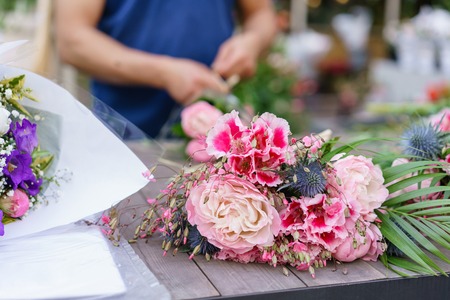 Male florist creating beautiful bouquet in flower shop. outdoor working in flower shop. Man assistant or owner in floral design studio, making decorations and arrangements.の写真素材