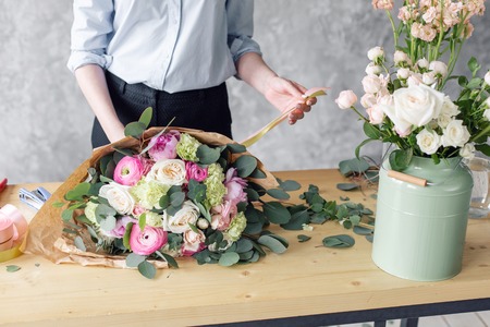 Woman florist creating beautiful bouquet in flower shop. Working in flower shop. Girl assistant or owner in floral design studio, making decorations and arrangements.の写真素材