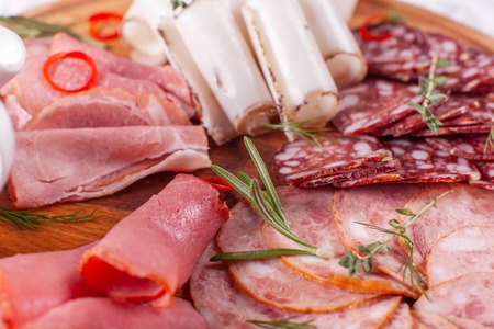 Food tray with delicious salami, pieces of sliced ham, sausage. Cutting sausage and cured meat on a...