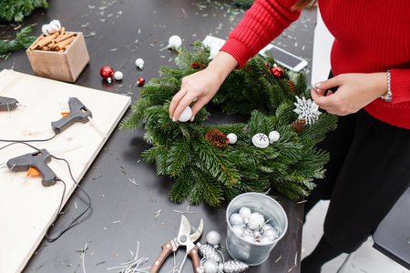 A woman decorates a Christmas wreath. Hands close-up. Master class on making decorative ornaments. Christmas decor with their own hands. The new year celebration. Flower shopの写真素材