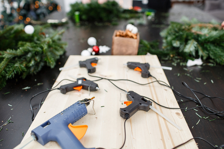 Several glue guns in the foreground on the Board. Manufacturer of Christmas wreath from branches of pine for holiday. Master class on making decorative ornaments.の写真素材