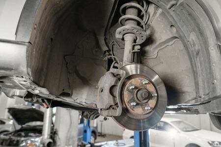 Car mechanic inspecting car wheel and repair suspension detail. Lifted automobile at repair service station. replacement of ferrule and leverageの写真素材
