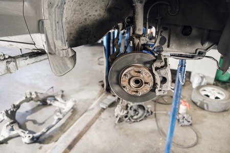 Car mechanic inspecting car wheel and repair suspension detail. Lifted automobile at repair service station. replacement of ferrule and leverageの写真素材