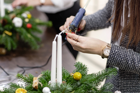 Woman decorated a Christmas wreath. Attaches toys and decor with glue gun. Hands close-up. Master class on making decorative ornaments. Christmas decor with their own hands. Flower shopの写真素材
