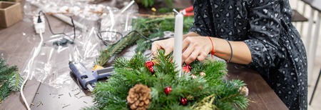 Woman decorated a Christmas wreath. Attaches toys and decor with glue gun. Hands close-up. Master...