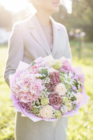 Young girl holding a beautiful spring bouquet. flower arrangement with hydrangea and garden roses. Color light pink. Bright dawn or sunset sunの写真素材