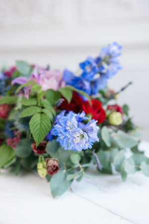 selective focus. Elongated floral arrangement in vintage metal vase. table setting. Blue and red color. Gorgeous bouquet of different flowers. Bright room, stucco on the wallの写真素材