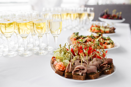 rye bread sandwiches, canapes, bruschetta on white plate. solemn banquet. Lot of glasses champagne or wine on the table in restaurant. buffet table with lots of delicious snacks.の写真素材