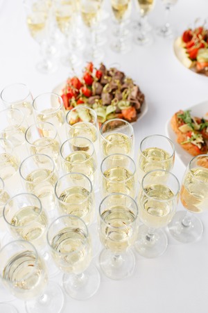 solemn happy new year banquet. Lot of glasses champagne or wine on the table in restaurant. buffet table with lots of delicious snacks. canapes, bruschetta, and little desserts on wooden plate boardの写真素材