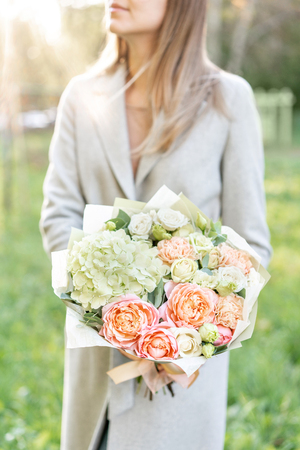 Close-up beautiful spring bouquet in hands. delicate flower arrangement with pink and green pastel color flowers. lawn on background. Bright dawn or sunset sun.の写真素材