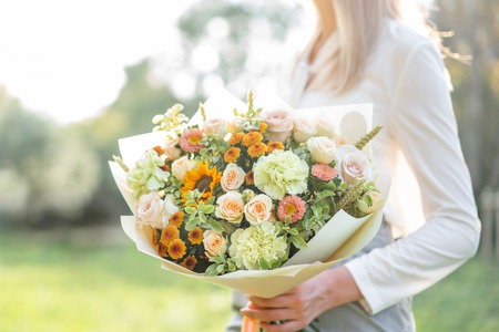 beautiful bouquet. Young girl holding a flowers arrangements with variety of colors. Bright dawn or sunset sunの写真素材