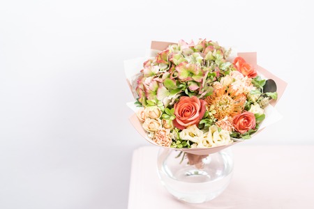 beautiful spring bouquet. flowers arrangement with various of colors in glass vase on pink table. bright room, white wall. copy spaceの写真素材