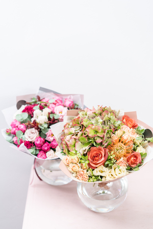 two beautiful spring bouquet. flowers arrangements with various of colors in glass vase on pink table. bright room, white wallの写真素材