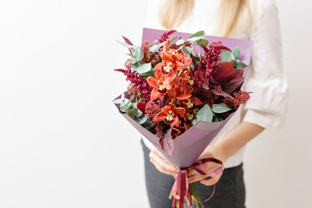 bouquet of orange Orchid and different flowers. Young girl holding a flowers arrangements with various of colors. white wall.の写真素材
