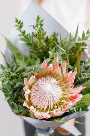 Lush bouquet of king Protea, eucalyptus and other greens. Young girl holding a flowers arrangements with various of colors. white wall.の写真素材