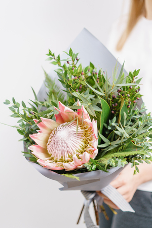 Lush bouquet of king Protea, eucalyptus and other greens. Young girl holding a flowers arrangements with various of colors. white wall.の写真素材