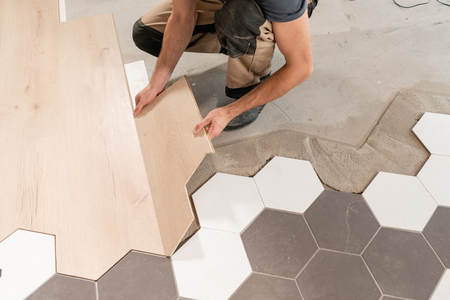 Male worker installing new wooden laminate flooring. The combination of wood panels of laminate and ceramic tiles in the form of honeycomb. Kitchen renovation.の写真素材