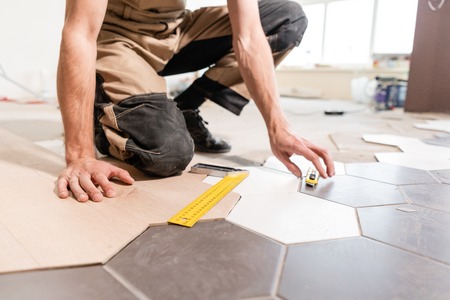 Male worker makes measurements and installing new wooden laminate flooring. The combination of wood panels of laminate and ceramic tiles in the form of honeycomb. Kitchen renovation.の写真素材