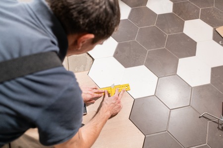 Male worker makes measurements and installing new wooden laminate flooring. The combination of wood panels of laminate and ceramic tiles in the form of honeycomb. Kitchen renovation.の写真素材