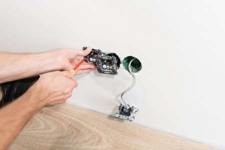 electrician connects the sockets to the electrical wires on wall in White room. Screwdriver, close-up electrician hands.の写真素材