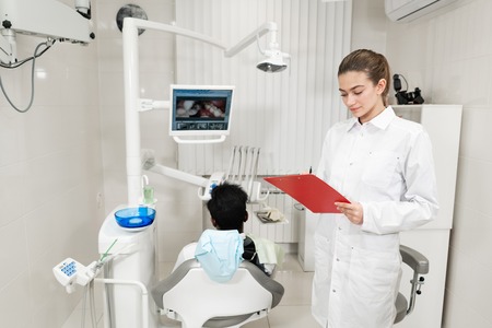 Charming beautiful girl doctor dentist. Young African American male patient at chair at dental clinic. Medicine, health, stomatology concept. dentist conducts inspection and concludes. Woman smilingの写真素材