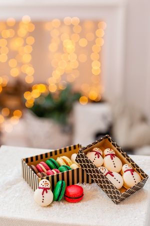Variety of sweet macaroons in carton box. Cookie in the form of a snowman. Merry Christmas card. New year mood. lights of garland bulbsの写真素材