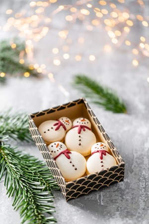 Variety of sweet macaroons in carton box. Cookie in the form of a snowman. Fir branches on a gray background. Merry Christmas card. New year moodの写真素材