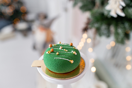 Mini mousse pastry dessert covered with green velour on garland lamps bokeh background. Modern european cake. French cuisine. Christmas themeの写真素材