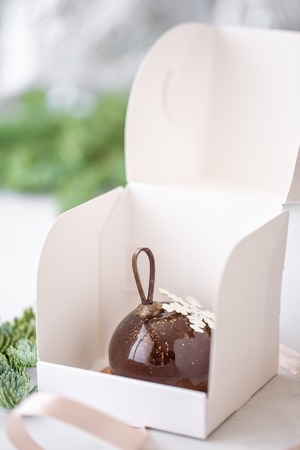 Mini mousse pastry dessert with chocolate glazed Individually wrapped in white box. The branches of spruce on bokeh background. Modern european cake. French cuisine. Christmas . Snowflakeの写真素材