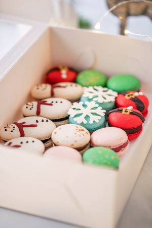 Variety of sweet macaroons in white box. The branches of spruce on bokeh background. Modern european French cuisine. Christmas theme, Merry Christmas card. New year mood. lights of garland bulbsの写真素材