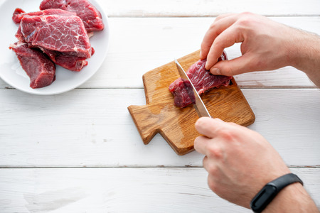 Closeup of the hands of a butcher cutting slices of raw meat off a large loin. Raw meat. Raw fresh beef steak on a wood cutting board and Carving knife.の写真素材