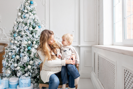 Happy family Portrait In Home - young pregnant mother embraces his little son. Happy new year. decorated Christmas tree. Christmas morning in bright living room.の写真素材