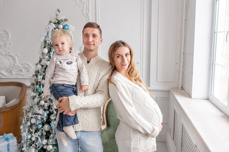 Happy family Portrait In Home - father, pregnant mother and their little son. Happy new year. decorated Christmas tree. Christmas morning in bright living room.の写真素材