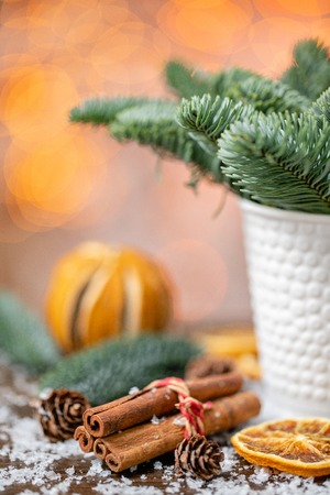 Cinnamon sticks and orange slicesChristmas arrangement with Norwegian pine Nobilis and decorated with toys. Garland bokeh on background. Dark wooden table sprinkled with snowの写真素材