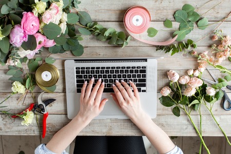 Close-up of hands, laptop keyboard and floral table. Woman blogger and content creators of social...