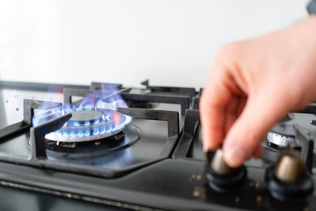 focus on fire. A man lighting the gas-stove with by means of automatic electric ignition. Modern gas burner and hob on a kitchen range. Dark black color and wooden Small kitchen in a modern apartmentの写真素材