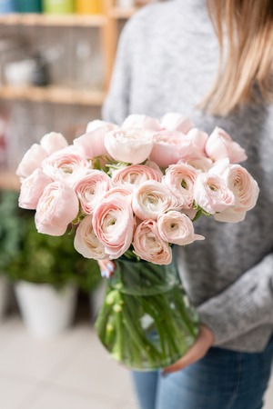 Persian buttercup in glass vases in womens hands. Bunch pale pink. the concept of a florist in a...