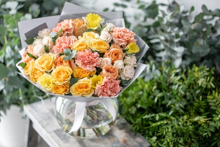 beautiful fresh cut bouquet of mixed flowers in vase on wooden table. The work of the florist at a flower shop. Delicate Pastel tones colorの写真素材