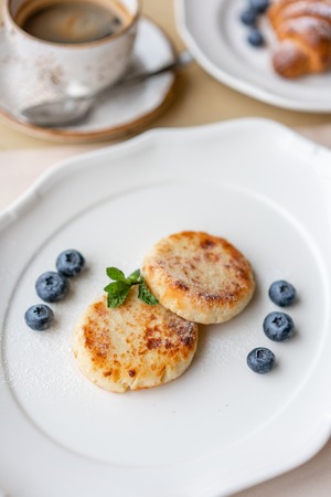 Cheesecake, fresh blueberry and cappuccino. Cottage cheese pancakes or curd fritters on white plate. Healthy and diet breakfast at sunriseの写真素材