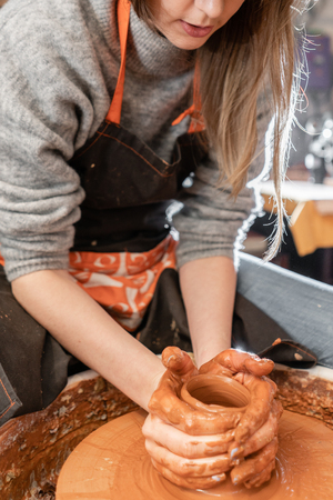 Happy woman working on potter wheel in pottery workshop. Family business shop sculpts pot from clay view top.の写真素材