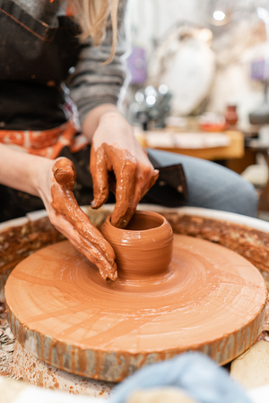 Craftsman hands making pottery bowl. Woman working on potter wheel . Family business shop sculpts pot from clay view top.の写真素材