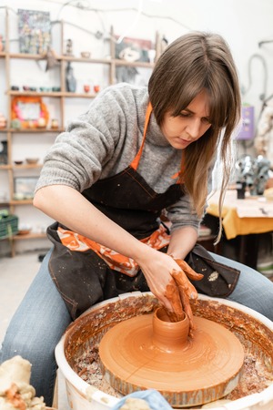Happy woman working on potter wheel in pottery workshop. Family business shop sculpts pot from clay view top.の写真素材