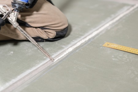 Worker is using a polyurethane foam for gluing drywall at ninety degrees. Hand holding polyurethane expanding foam glue gun applicatorの写真素材