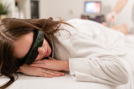 Doctor cosmetologist makes the procedure a young girl brunette. Laser epilation and cosmetology. Hair removal on ladies legs. at cosmetic beauty spa clinic.の写真素材