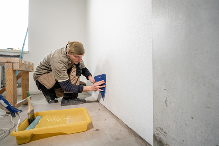 Young man, worker glueing wallpapers on concrete wall. Repair the apartment. Home renovation concept. White Wallpaper for paintの写真素材